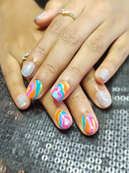 Your nails are your canvas. This fun and vibrant design features a playful rainbow marble effect on some nails, perfectly balanced with a sparkling silver glitter polish on others.