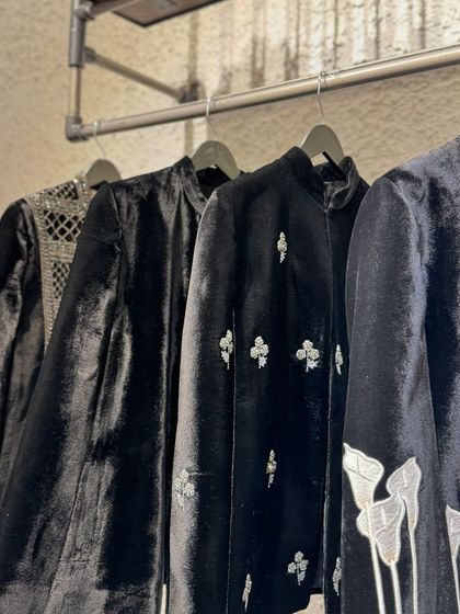 A rack of elegant black velvet jackets and capes, featuring various styles of silver and white embroidery.