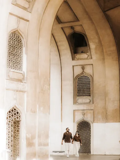 The couple walks hand-in-hand through a corridor of stunning arches. The light and shadow play beautifully, creating a sense of depth and history in this heritage location portrait.