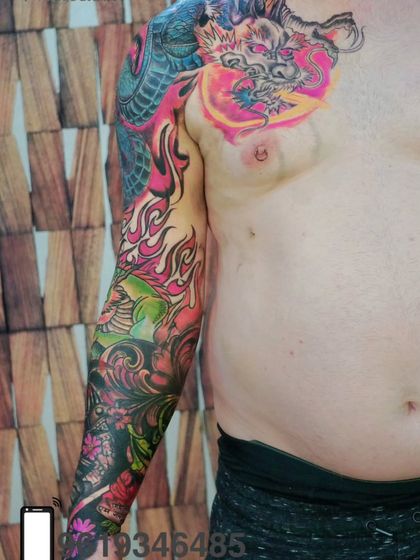 A full sleeve and chest tattoo in a vibrant, Japanese-inspired style. This colorful piece features a dragon and flames, covering a large area of the body with stunning art.