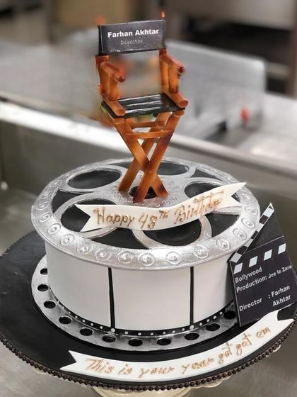 A film themed cake designed for Farhan Akhtar's 48th birthday. The cake is shaped like a film reel, complete with a director's chair and clapboard, celebrating his incredible work in cinema.