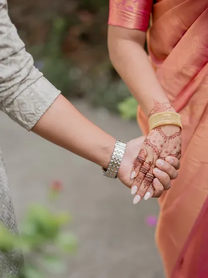 A candid shot of the couple holding hands, showing off the beautiful engagement mehendi. It's these little moments that make the celebration so special.