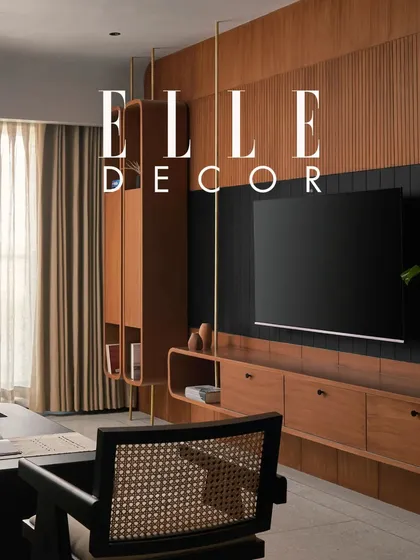 Another shot from the Elle Decor feature, this image highlights the custom floating shelving unit and TV console. The design uses natural teak wood and brass verticals to add texture and warmth, creating a functional yet beautiful focal point in the living area.