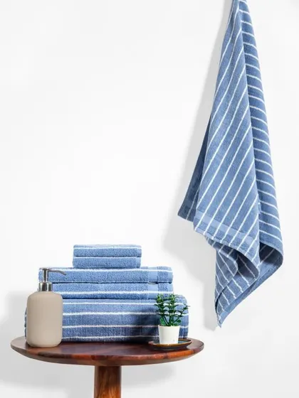 A clean and simple product shot of a towel set. The minimalist styling with a small plant and soap dispenser on a wooden table creates a serene, spa-like bathroom setting.