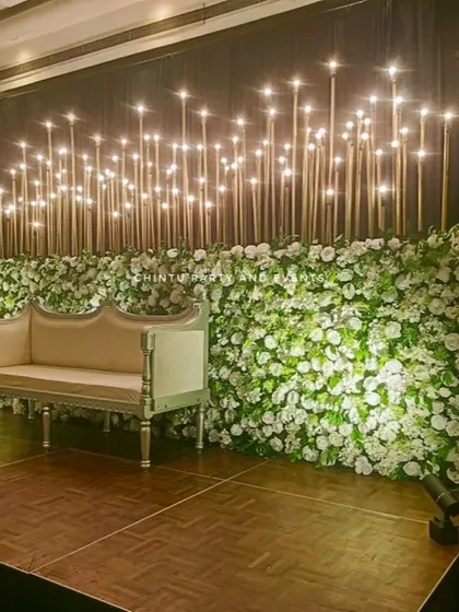 A modern Christian wedding stage with a wall of white flowers. The backdrop is dramatically lit from above with dozens of hanging lights.