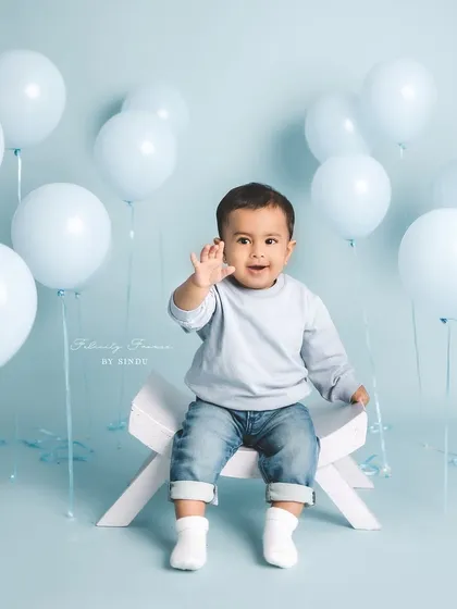 A happy wave from this little guy during his milestone session. The light blue balloons create a fun and celebratory atmosphere for his portraits.