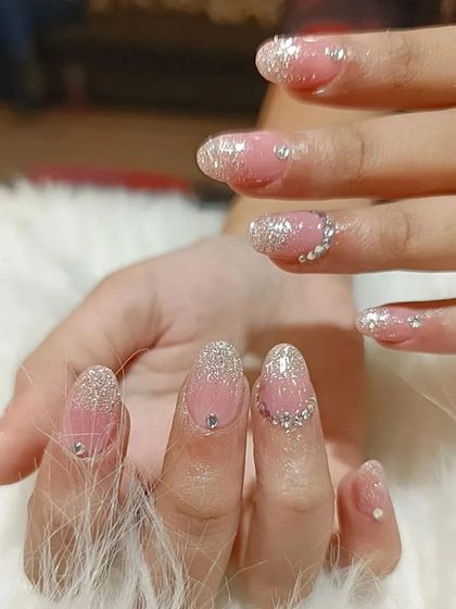 A glamorous set of pink nails with a heavy silver glitter fade from the tip, accented with rhinestones at the cuticle.
