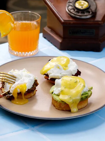 The perfect #yolkporn moment. A fork pierces a poached egg, releasing a runny golden yolk over eggs benedict.