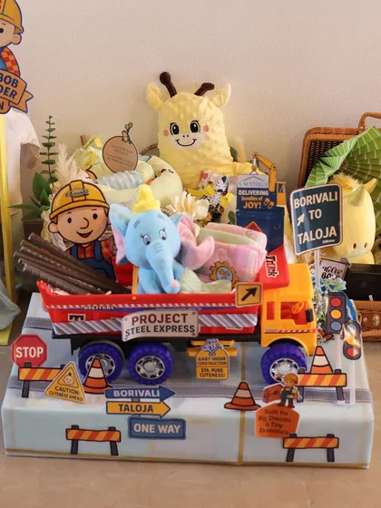 The full view of the 'Project Steel Express' hamper. It features a Bob the Builder cutout, a toy truck filled with gifts, and custom road signs pointing to Borivali and Taloja, adding a personal touch for the family.