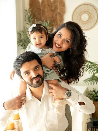 A fun and playful family portrait celebrating a first birthday. Capturing the joy on everyone's faces, with the birthday girl enjoying a ride on her daddy's shoulders, makes for a cherished memory.