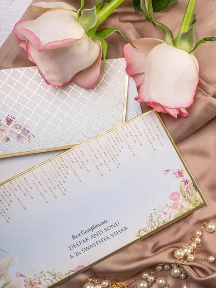A romantic, softly lit shot of wedding stationery, styled with pink roses and pearls. This composition is perfect for luxury wedding invitation designers.