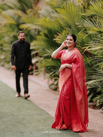 The groom, Antony, approaches his bride, Jesna, in a garden setting. Her radiant smile as she looks back at him is a picture of pure happiness.