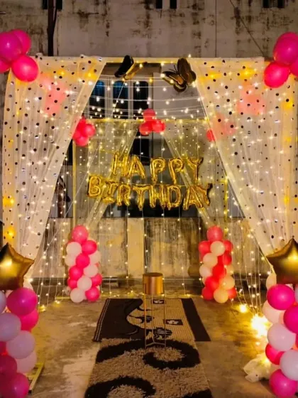 A terrace decoration with a fairy light curtain, "Happy Birthday" banner, and pink and white balloon columns.