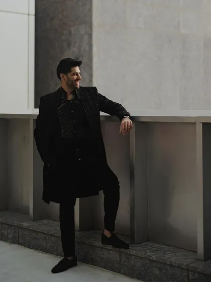 A confident portrait of the groom in a stylish all-black ensemble. His relaxed pose and the modern architectural background give this shot a cool, contemporary vibe.