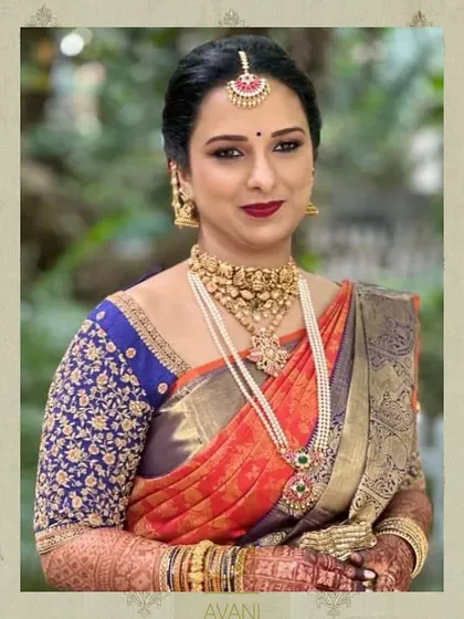 A bride in a multi-colored saree with a royal blue blouse. The blouse is heavily embroidered with floral motifs, adding a rich texture to the overall look.