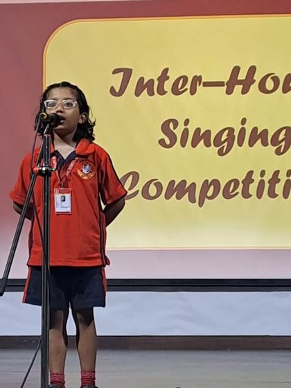 A young girl in her red house t-shirt performs with focus during the singing competition.
