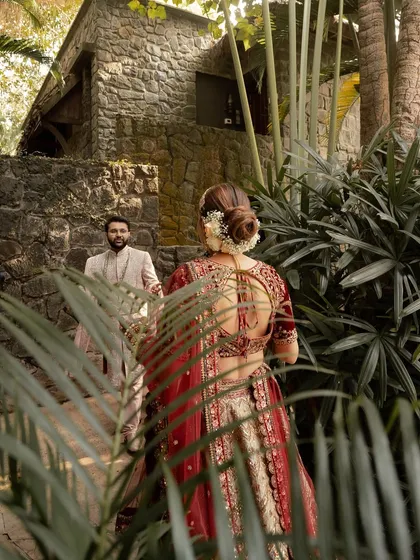 A creative "first look" shot, with the groom waiting as the bride approaches, seen through the foliage. It builds a sense of anticipation and romance.