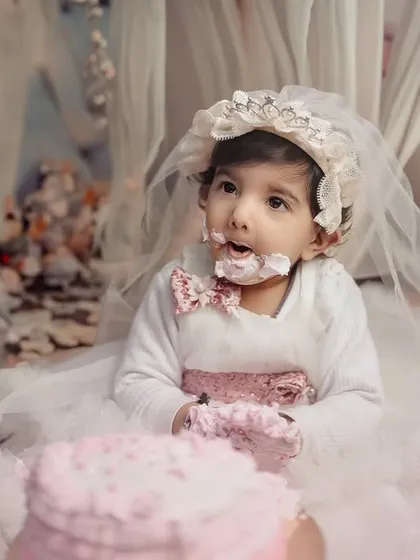 A sweet and gentle cake smash for a little princess. Dressed in a beautiful white gown and bonnet, she delicately explores her very first birthday cake in a dreamy, floral setting.