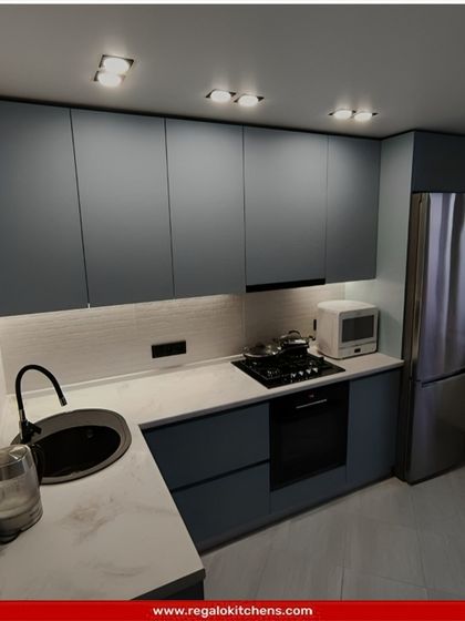 A compact and modern L-shaped kitchen in a cool blue-grey tone. The design is simple yet effective, with a round black sink and integrated appliances making it a perfect fit for a smaller apartment or home.