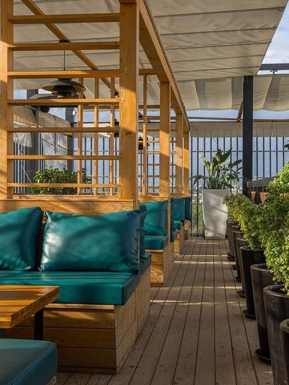 For this rooftop bar, we designed comfortable cabana-style seating with wooden frames and plush teal cushions. The retractable fabric roof provides shade during the day, creating a perfect spot for relaxed conversations.