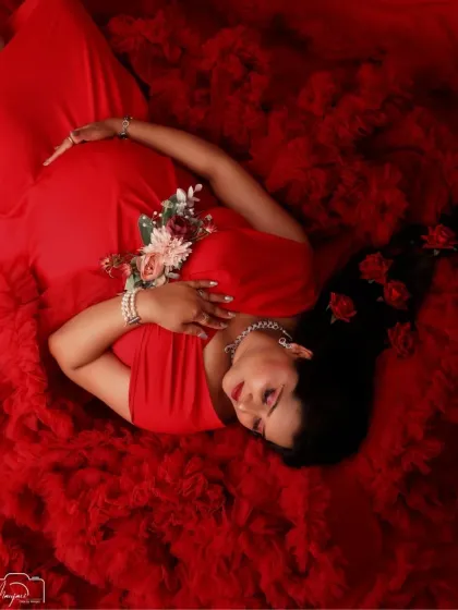 Lost in a dream of red. This peaceful sleeping pose, surrounded by the rich texture of the gown and delicate roses, creates a timeless and romantic maternity portrait.