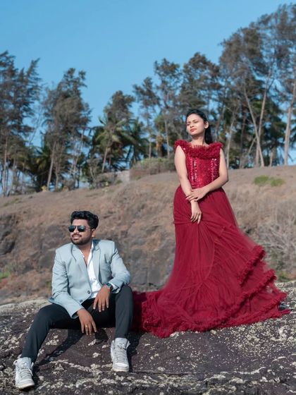 A stylish pre-wedding shot on the rocks. The bride-to-be looks effortlessly cool in a ruffled red gown, posing with her partner.