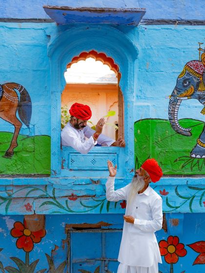 Two men in red turbans interact through a beautifully painted window in Jodhpur. The colorful murals of elephants and flowers add to the storybook feel of the city.
