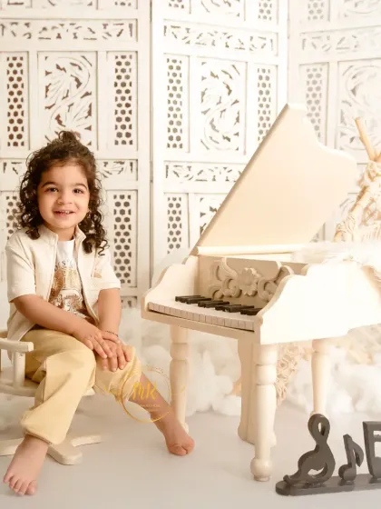 A toddler boy sits next to a miniature piano, a fun prop that encourages playful and natural expressions.