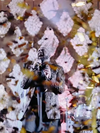 A moment of musical bliss during a Sufi night. A shower of petals rains down on the lead singer as he captivates the audience, his voice echoing through the hall against a backdrop of white floral latticework.