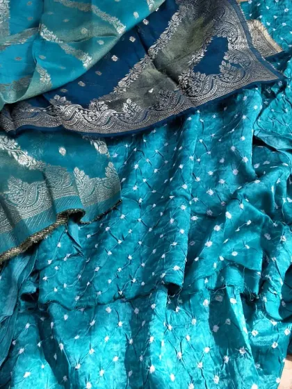 A close-up of the beautiful Banarasi Bandhej fabric in a vibrant teal color. The intricate weaving and the delicate bandhej dots create a stunning texture.