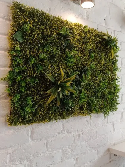 An artificial vertical garden doesn't have to cover the whole wall. This framed green panel acts as a piece of living art against the white brick wall, with spotlights to highlight its texture.