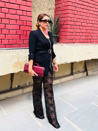 A full view of the black blazer and lace pants ensemble. The belt cinches the waist, creating a flattering silhouette, while the flared lace pants add a touch of drama and elegance.