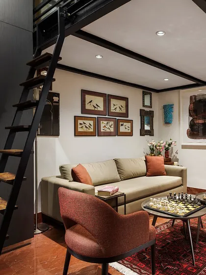 A small sitting room that serves as a cozy hub, featuring a loft bed accessible by a ladder. The walls are a memory gallery, displaying 19th-century ornithological watercolors, small mirrors from travels, and contemporary art.
