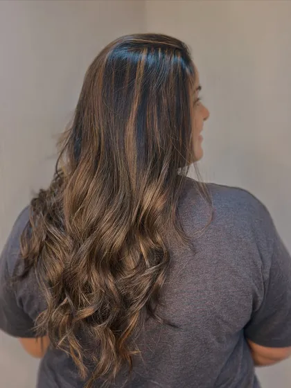 Warm tones for the win. This balayage adds a beautiful, rich warmth to her hair, styled in loose waves for a relaxed, beachy vibe.