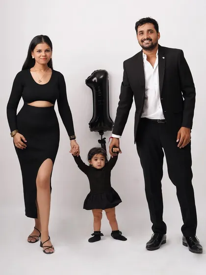 A stylish family portrait celebrating a first birthday, with the parents and child dressed in black, holding hands and smiling.