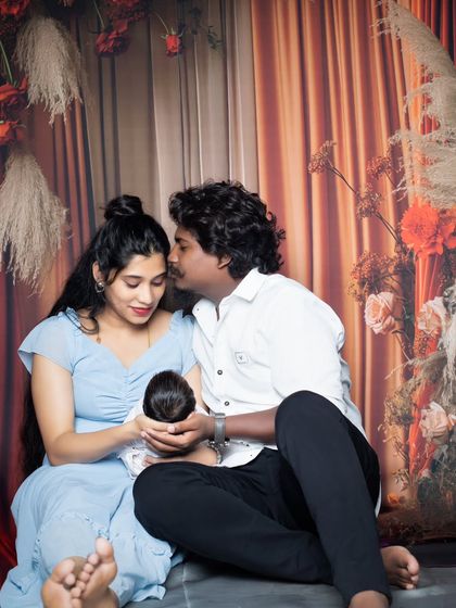 A candid moment of a new father kissing his partner's head while she holds their sleeping newborn.