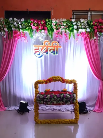 A simple and elegant naming ceremony backdrop. A decorated floral jhula is placed in front of white and pink drapes, with the baby's name highlighted.