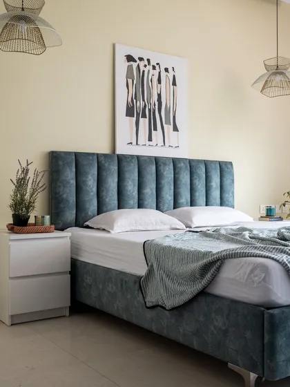 A simple yet sophisticated bedroom featuring a channel-tufted headboard in a calming blue fabric. The look is completed with minimalist white nightstands and woven pendant lights that add a touch of warmth.