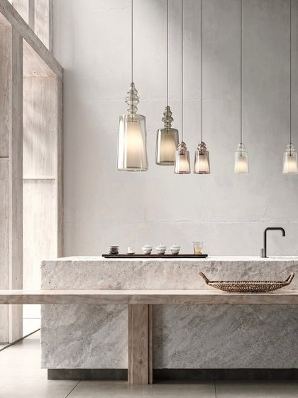 A linear arrangement of Alibaglass pendants in different sizes creates a beautiful, cascading effect over a long stone counter, perfect for a modern kitchen or bar.