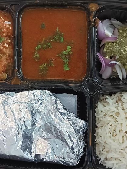 This thali features two unique dishes: black chole and baingan bharta (roasted eggplant mash). It's a rustic and authentic meal full of smoky flavors.