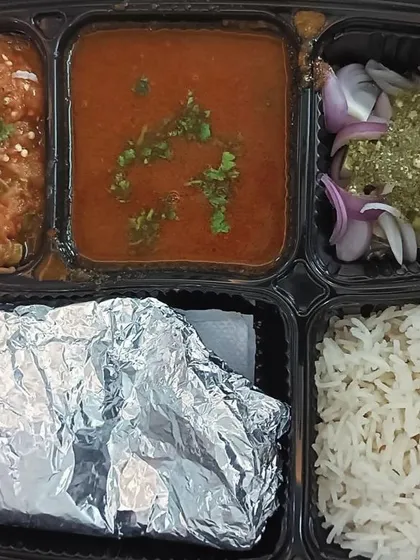 This thali features two unique dishes: black chole and baingan bharta (roasted eggplant mash). It's a rustic and authentic meal full of smoky flavors.