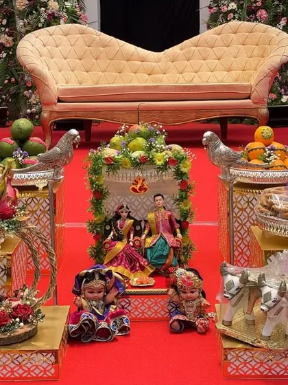 A close-up of a plate decoration setup featuring a central doll scene of a couple. The arrangement also includes miniature dolls and a decorative bullock cart, adding a narrative element to the decor.