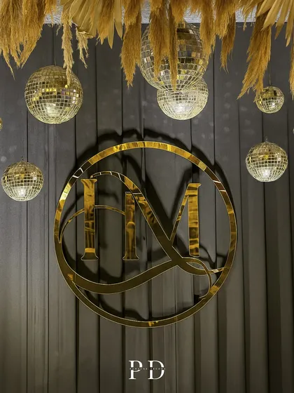 A detail shot of the custom monogram and disco ball arrangement. The mix of metallic gold and natural pampas grass creates a modern, boho-glam aesthetic.