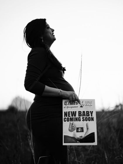 A hopeful and uplifting black and white portrait. The mom-to-be looks towards the sky, proudly holding her announcement newspaper.