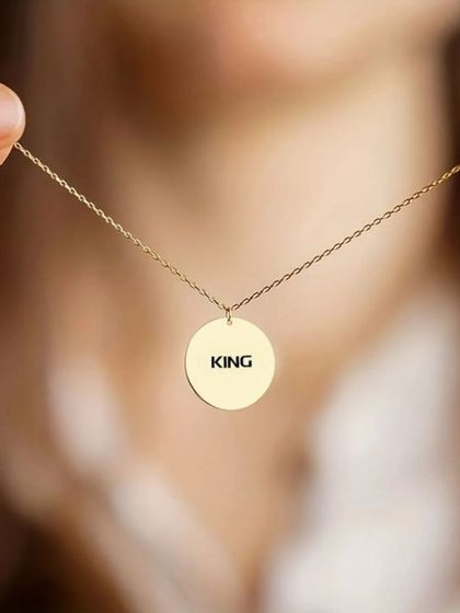 A simple gold round pendant engraved with the word 'KING'. This demonstrates how a single powerful word can create a strong statement piece.