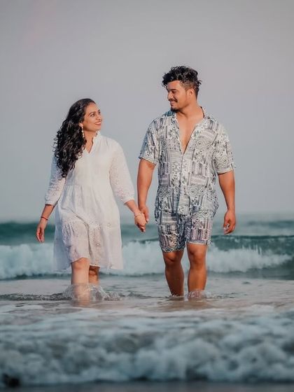A candid shot of a couple walking hand-in-hand through the ocean waves. Their casual outfits and the natural setting create a relaxed and authentic pre-wedding photo.