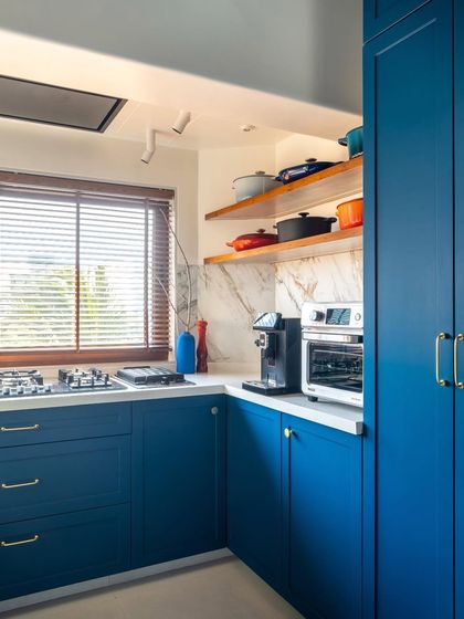 This view highlights the functionality of the dry kitchen area. We used the same bold blue for the cabinetry, contrasted with a clean white countertop and marble backsplash. Open wooden shelves provide practical storage while adding a warm, natural element.