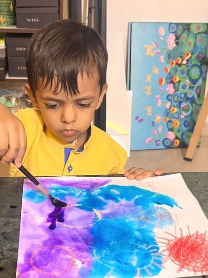 With great concentration, this little boy applies purple watercolor to his artwork, watching the colors flow.