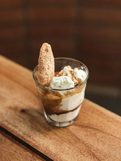An affogato in the making. A scoop of vanilla ice cream in a glass with a ladyfinger, waiting for a shot of hot espresso to be poured over.