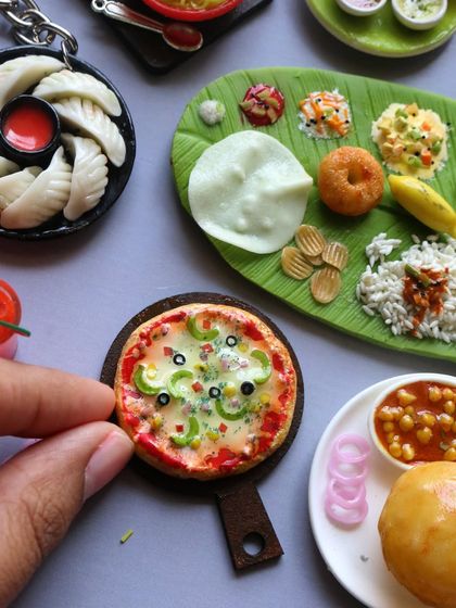 A close-up of a pizza miniature next to a chole bhature and a South Indian meal.
